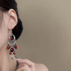 Detail of vintage bohemian tassel earrings with red beads and silver leaf pendant on model