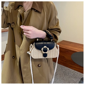 Détail d'un sac en paille tressée avec fermoir fleur doré et rabat en cuir noir