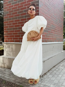Détail d'une robe blanche en coton à manches bouffantes et jupe fluide sur brique