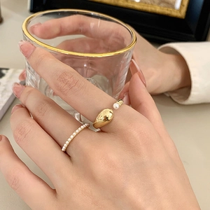 Detail of two-piece gold plated rings featuring delicate pearls on a hand holding a glass