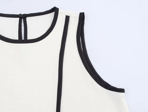 Detail view of white sleeveless top showing black contrast piping on neckline and armhole