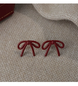 Macro detail of deep red bow earrings on beige knit texture with gift box
