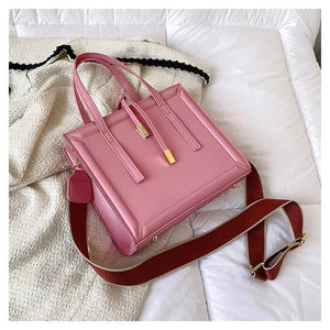 Pink square handbag with gold hardware and wide contrast strap on cream cardigan