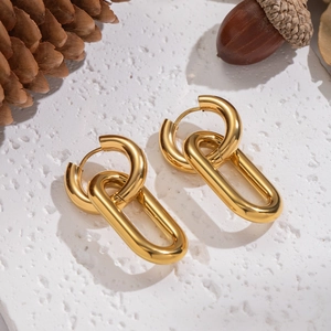 Close-up of dual-tone 18K gold earrings on textured white surface with pine cones