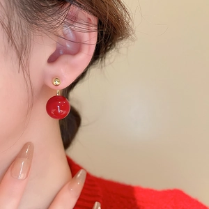 Close-up of red high-gloss pearl earring with gold plating worn by a model