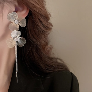 Détail de boucles d'oreilles à pompons argentés avec fleurs et strass sur un mannequin