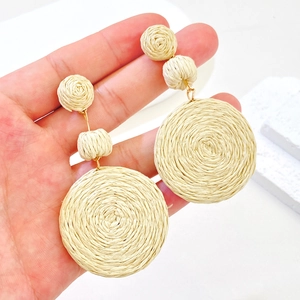 Detailed view of handmade beige raffia woven earrings with geometric round shapes
