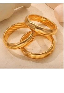 Close-up of three golden Tubogas style spiral stainless steel bracelets on a stone surface