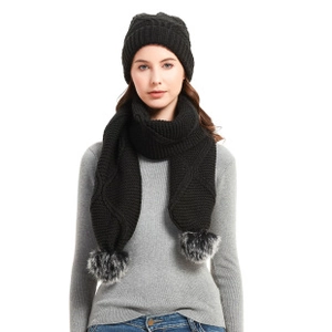 Detail of black knitted scarf and hat set featuring soft grey faux fur pom-poms on ends