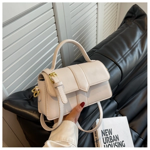 Detail of white PU leather handbag with top handle and gold hardware in urban setting
