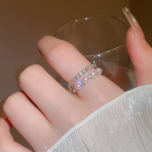 Detail view of a double-layered gold ring with pearls and crystals worn on model's hand