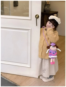 Detail of a purple handmade knit doll crossbody bag worn with a yellow cardigan