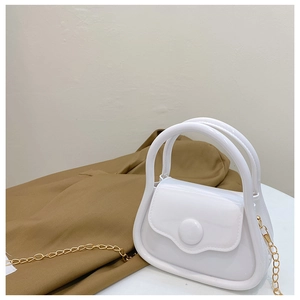 Detail of white glossy mini jelly bag with gold metal chain and top handle on table
