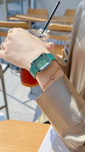 Close-up of a green leather rectangular watch with silver case and matching bracelet