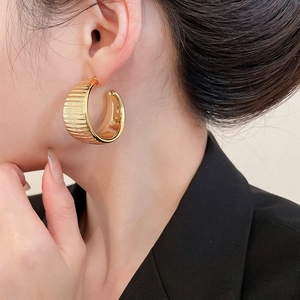 Macro view of gold C-shape hoop earrings featuring a vertical textured metal surface
