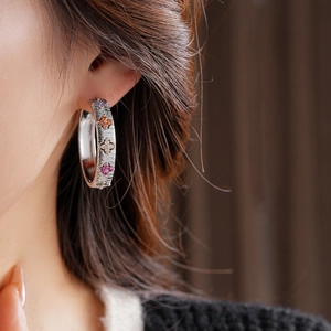 Gros plan sur des boucles d'oreilles trèfle en argent avec zircons colorés portées