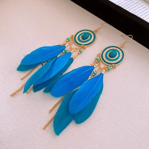 Détail de boucles d'oreilles bohèmes en plumes bleues avec résine turquoise et chaîne dorée