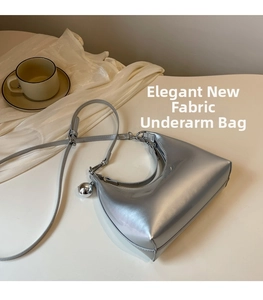 Detail of silver metallic hobo bag with adjustable strap and metal ball pendant on white surface