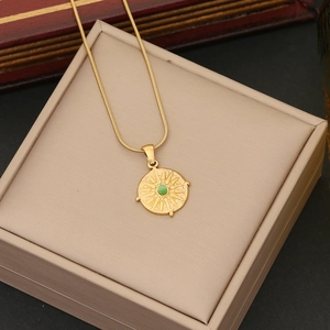 Close-up of gold snake chain necklace with green stone compass pendant on jewelry box