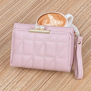 Close-up of pink quilted faux leather wallet with pearl clasp and hand strap on wood