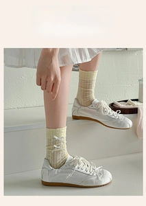 Detail of cream lace-knit crew socks with ribbon bow accents and breathable patterns