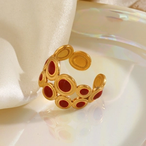 Gold geometric ring with red enamel circles on a soft white silk and ceramic background