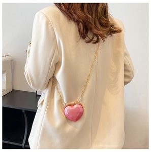 Close-up of a pink heart-shaped mini bag with gold chain strap on a beige suit