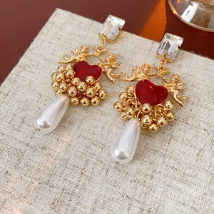 Close-up of vintage gold angel relief earrings with red heart and white pearl tassels