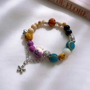 Detail of colorful ceramic beaded bracelet with floral charms on a soft fabric background