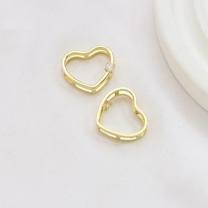 Macro detail of gold-plated hollow heart charms with clear zircon on soft white fabric