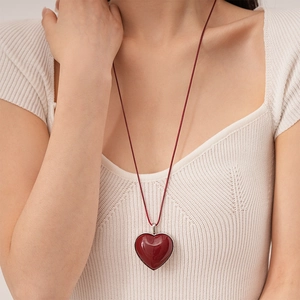 Close-up of a glossy deep red heart pendant necklace with silver trim on a white sweater