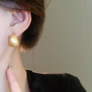 Close-up of golden teardrop earrings with a brushed matte texture worn by a model