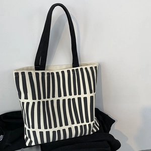 Detail of minimalist cream canvas tote bag featuring bold black vertical stripes and straps