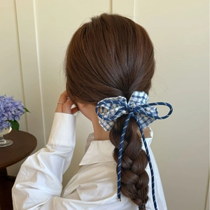 Blue plaid bow hair scrunchie with long tassels worn by a model in a cozy home setting