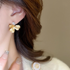 Close-up of elegant gold flower earring with central zircon on model's ear