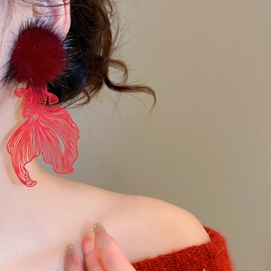 Detail of red hollow koi fish earring with plush ball shown on model in red sweater