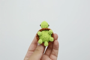 Dettaglio di una mini tartaruga all'uncinetto fatta a mano verde e marrone da borsa