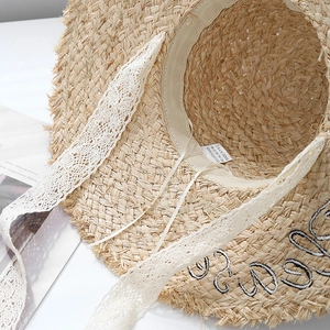 Macro detail of raffia straw hat featuring white lace ribbons and black letter embroidery