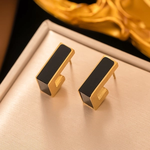 Close-up of geometric gold metal earrings with black rectangular inlay on silk background