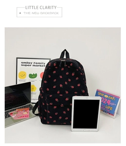 Close-up of black corduroy backpack with red strawberry embroidery on a desktop background