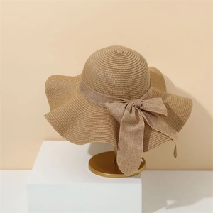Elegant beige straw sun hat with wide wavy brim and ribbon bow on display stand