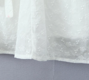 Detailed close-up of white cotton fabric featuring intricate floral embroidery and wavy patterns