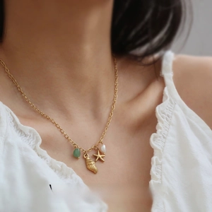 Detail of gold starfish, seashell, green bead and pearl charms on a dainty necklace