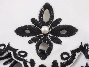 Macro detail of faux pearl embroidery on white fabric with black floral stitching