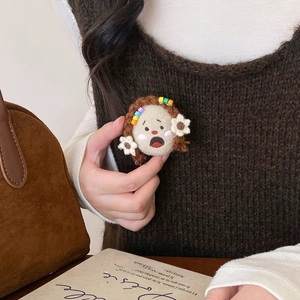 Handmade crochet cartoon girl brooch with braided hair on a brown knitted sweater