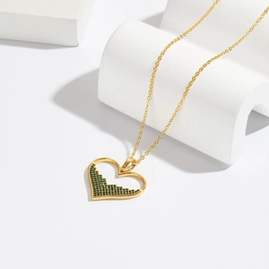 Elegant 18K gold heart necklace with emerald green gemstone on a white pedestal
