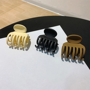 Three matte hair claw clips in beige, black and khaki colors on minimalist background