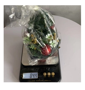 Close-up of a mini Christmas tree with red berries being weighed on a scale