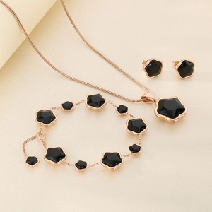 Detail of rose gold clover jewelry set with black enamel inlay and tassel accents