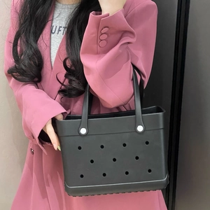 Detail of medium black EVA beach bag with holes held by a model in a pink suit